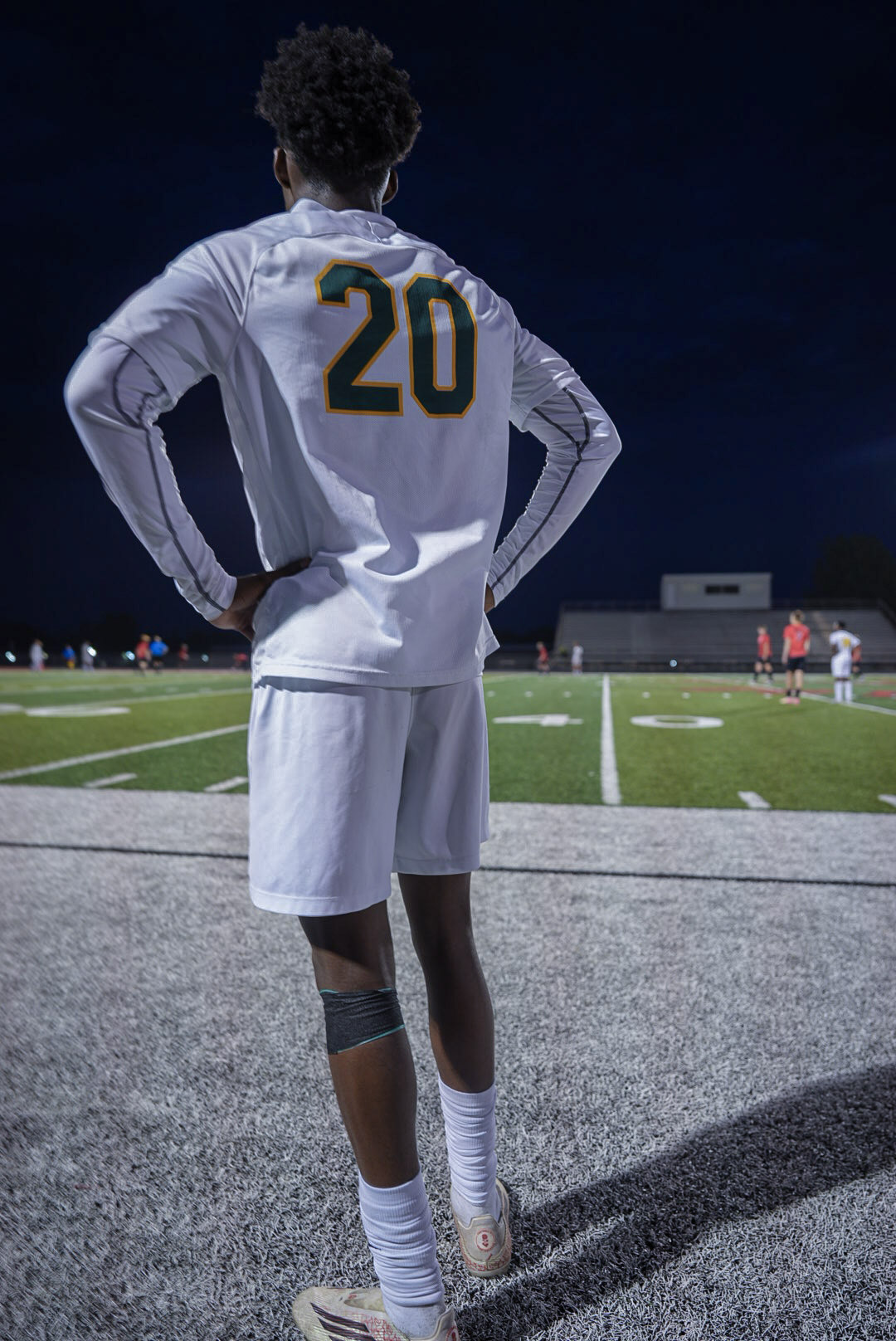 Soccer player number 20 watching the match from the sideline under stadium lights