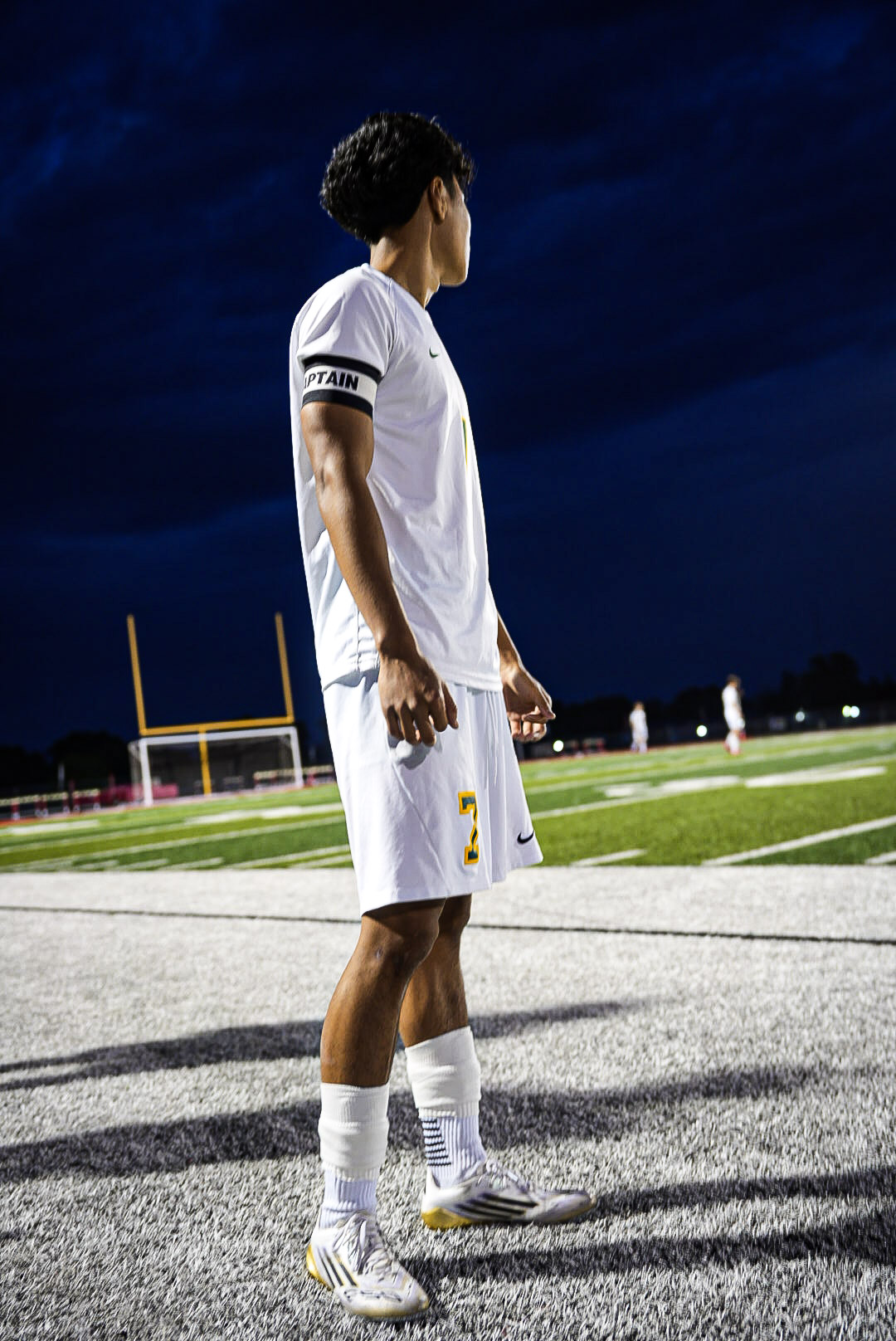 Soccer captain number 7 standing on the sideline with the goal behind him