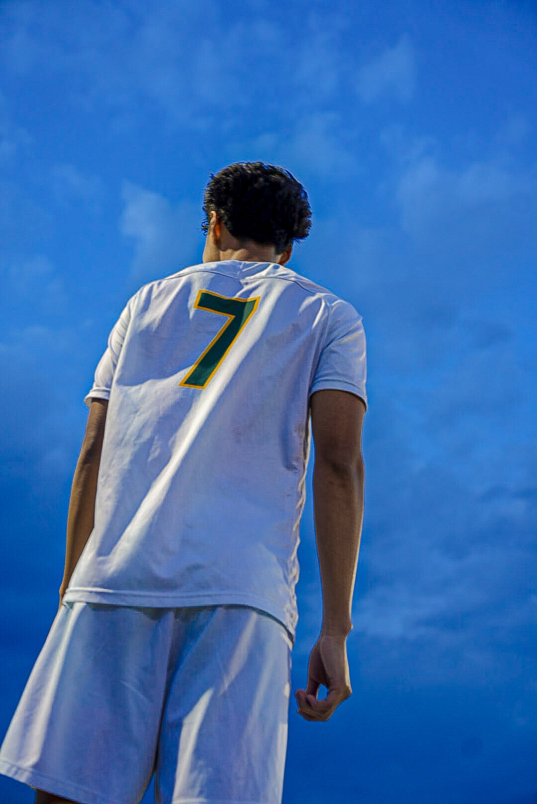 Soccer player number 7 photographed from below against a deep blue evening sky